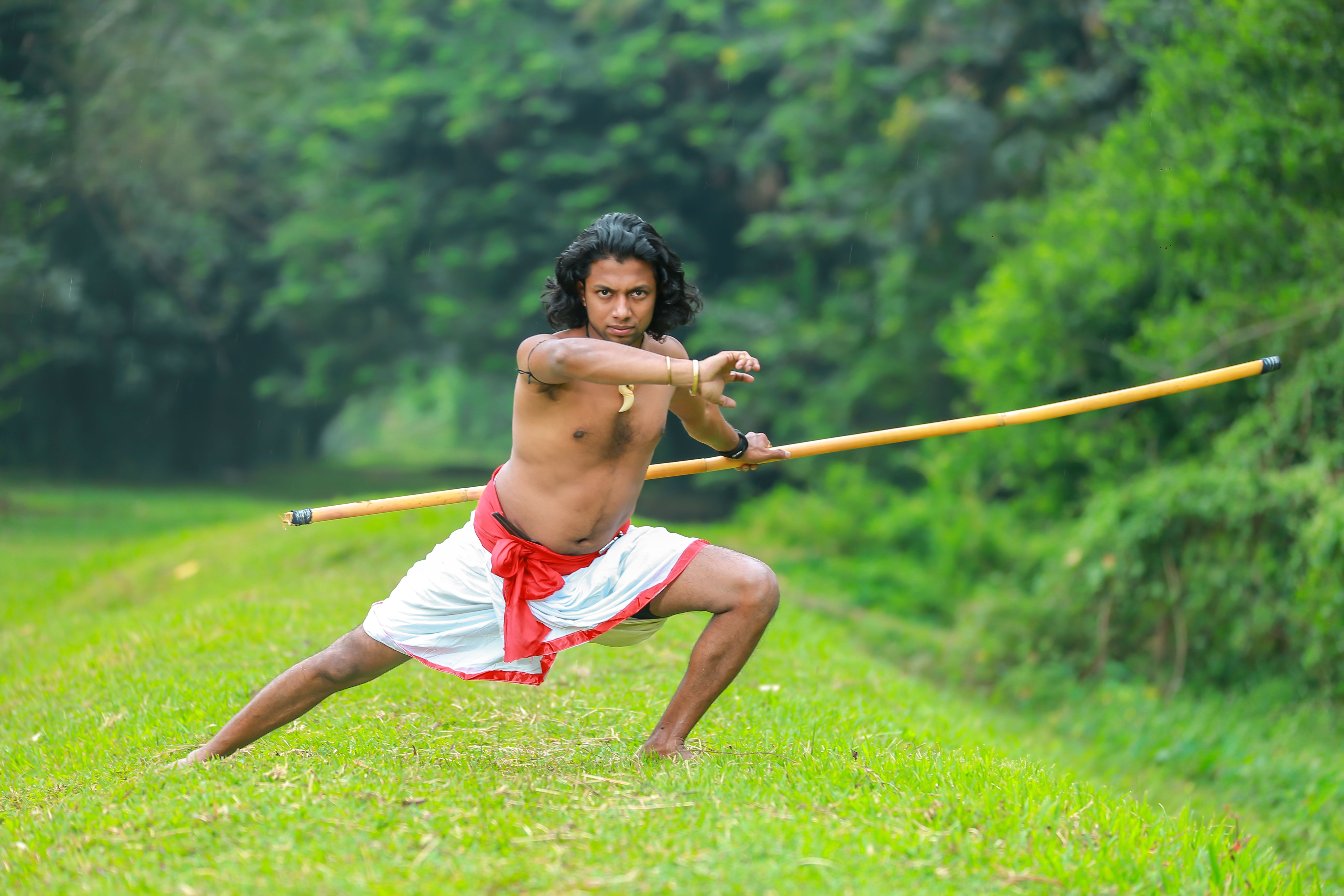 Kalaripayattu warrior with staff in a lush green setting